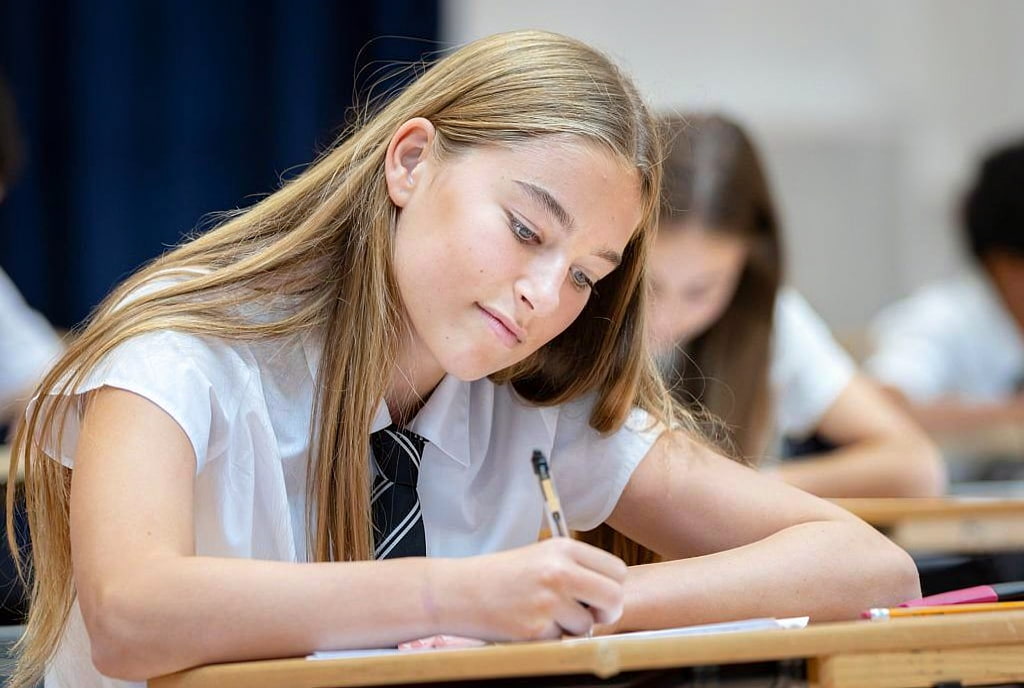 female high school student in a uniform writing at her desk during an exam