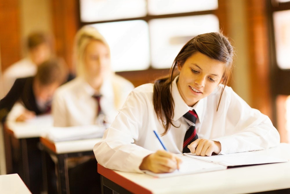 female high school student wearing a uniform and writing in a classroom exam